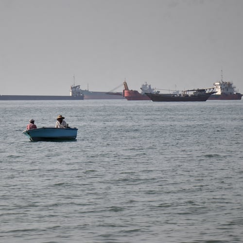 Two men sit in a small boat on the water as a mix of bulk carriers, cargo ships, and service vessels line the horizon in the Strait of Hormuz off Bandar Abbas, Iran, Monday, April 27, 2026.(Razieh Poudat/ISNA via AP)