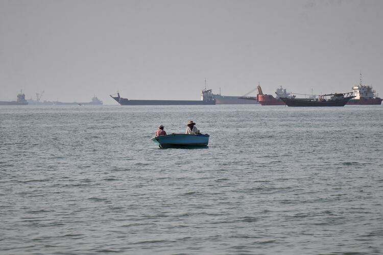 Two men sit in a small boat as a mix of bulk carriers, cargo ships and service vessels line the horizon in the Strait of Hormuz off Bandar Abbas, Iran, on Monday, April 27, 2026. The shipping channel may affect our markets, but the struggle inside Iran speaks to something even greater, guest columnist Batool Zamani writes. (Razieh Poudat/ISNA via AP)