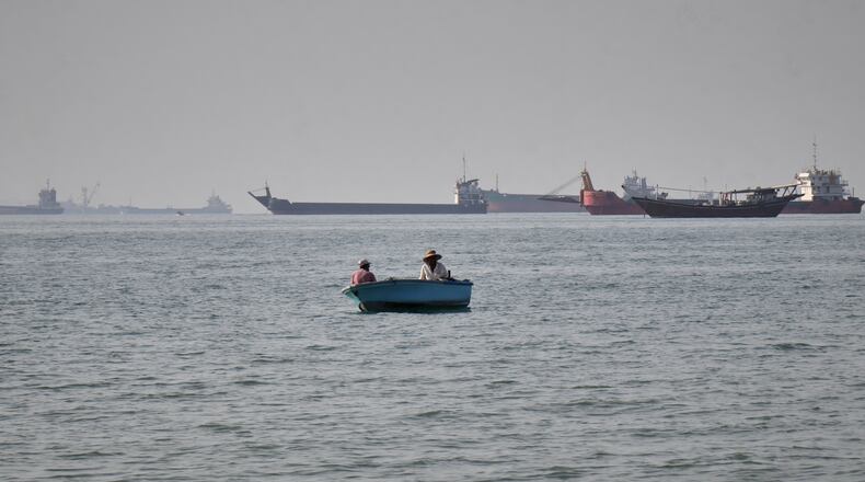 Two men sit in a small boat on the water as a mix of bulk carriers, cargo ships, and service vessels line the horizon in the Strait of Hormuz off Bandar Abbas, Iran, Monday, April 27, 2026.(Razieh Poudat/ISNA via AP)