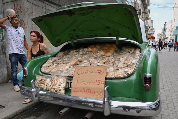 Vendors wait for customers next to the trunk of their American classic car stuffed with homemade crisps and bread, in Havana, Cuba, Tuesday, July 15, 2025. (AP Photo/Jorge Luis Baños)