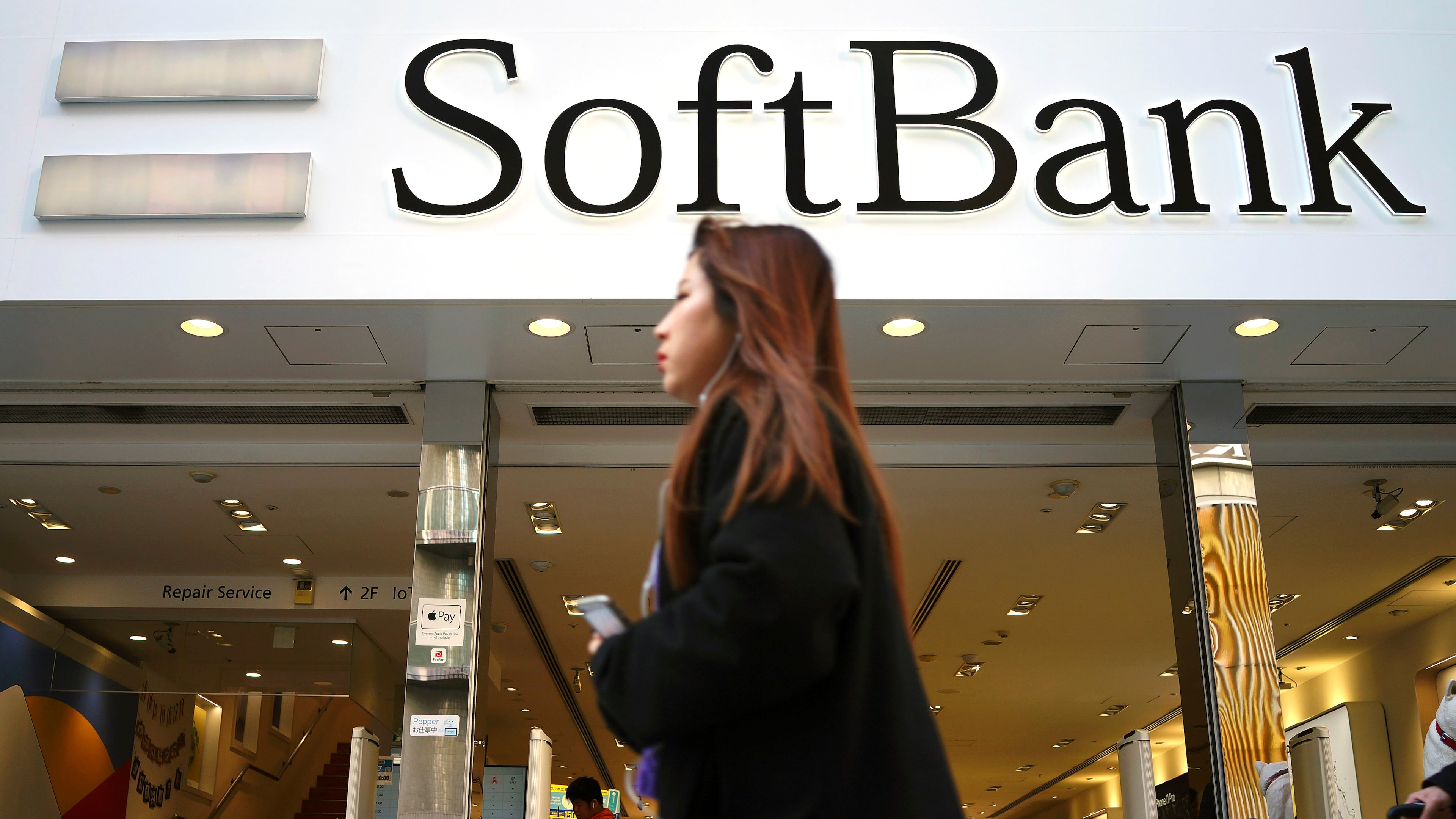 FILE - A woman walks in front of SoftBank store in Ginza shopping district in Tokyo, Jan. 20, 2020. (AP Photo/Eugene Hoshiko, File)