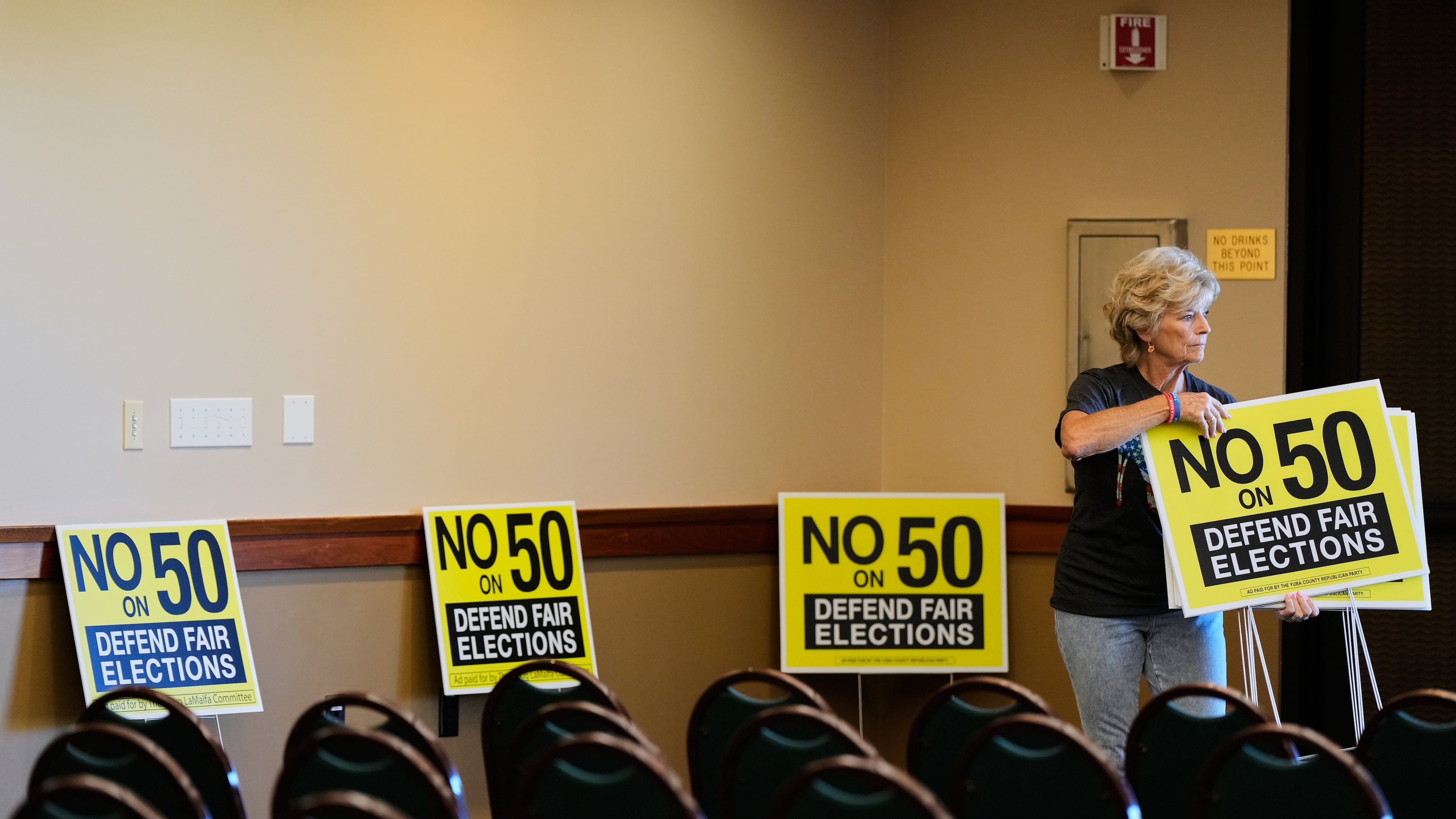 Brenda Haynes places signs throughout a conference room before a No on Prop 50 rally in Redding, Calif., Tuesday, Oct. 21, 2025. (AP Photo/Godofredo A. Vásquez)