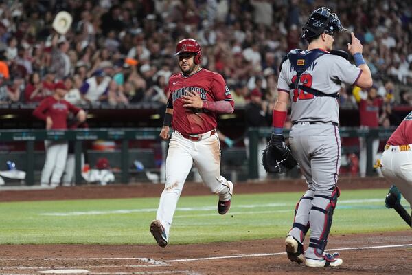 Arizona Diamondbacks' Eugenio Suárez, left, scores a run as Atlanta Braves catcher Sean Murphy, right, watches for the ball during the fourth inning of a baseball game Friday, April 25, 2025, in Phoenix. (AP Photo/Ross D. Franklin)