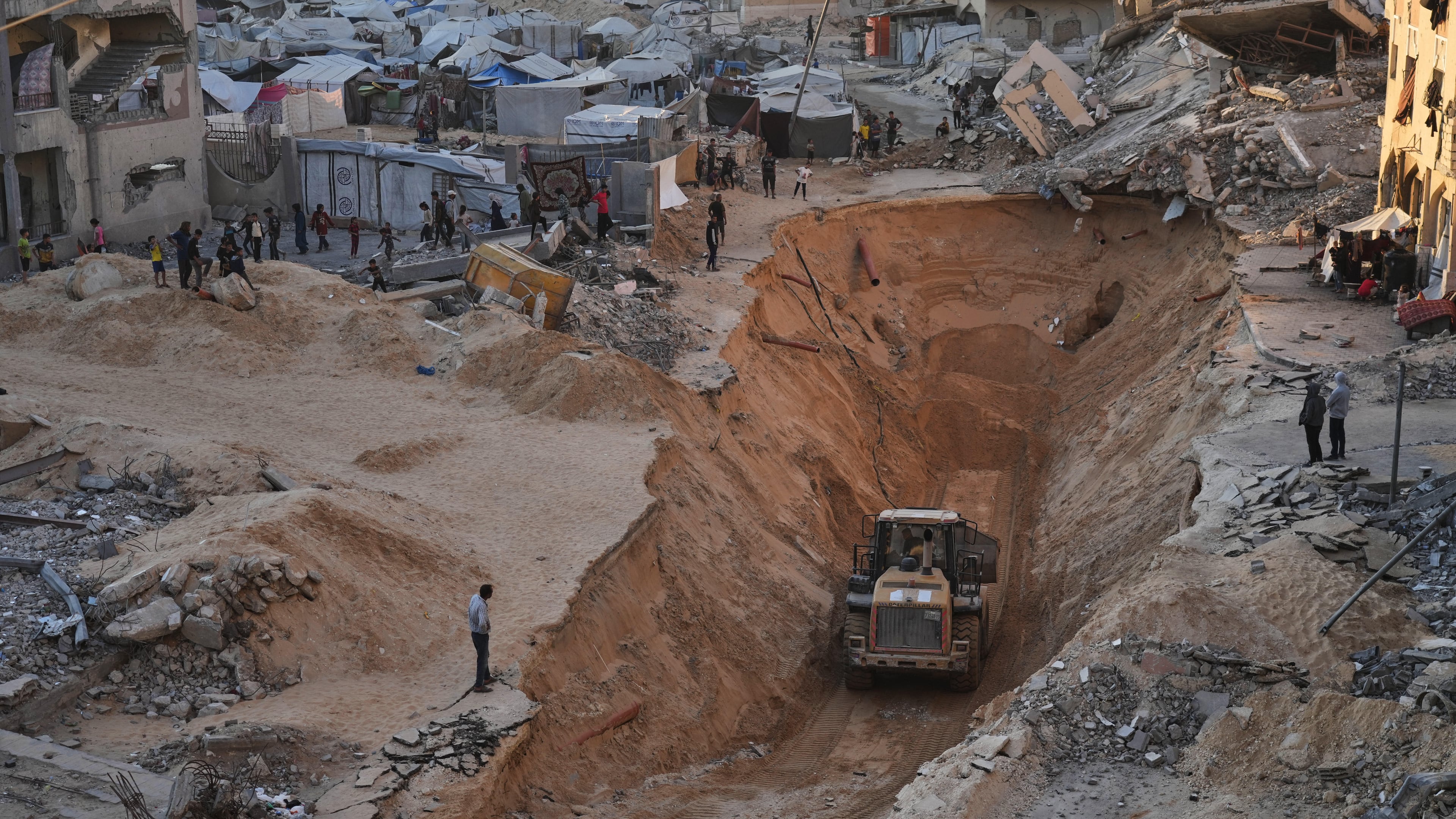 Palestinians watch members of the Hamas militant group searching for bodies of the hostages in Khan Younis, southern Gaza Strip, Saturday, Oct. 18, 2025. (AP Photo/Jehad Alshrafi)