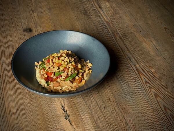 A dark plate filled with a field pea and peanut salad sits on a rustic wood surface.