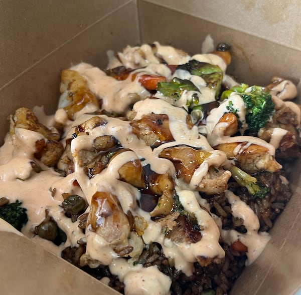 A cardboard carry-out container is filled with a mushroom rice dish and drizzled with a sauce. There is a little herb garnish on top.