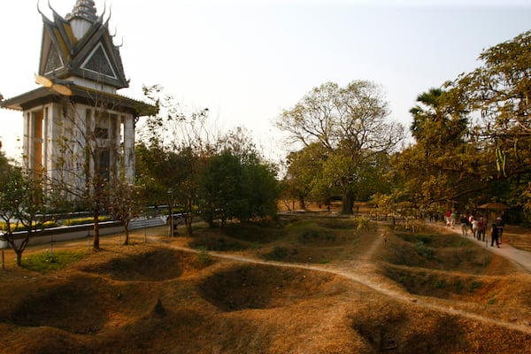 FILE - Visitors walk by the mass grave of the victims of the Khmer Rouge regime next to a memorial stupa filled with victims' skulls at the Choeung Ek killing field in Phnom Penh, Cambodia, Wednesday, Feb. 19, 2014. (AP Photo/Heng Sinith, File)