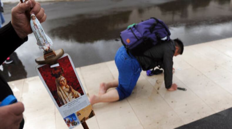 A pilgrim holds a staff decorated with images of Our Lady of Fatima as another walks on his knees paying penance at the Fatima Sanctuary, in Fatima, Portugal, Thursday, May 11, 2017. Pope Francis is visiting the Fatima shrine on May 12 and 13 to canonize two Portuguese shepherd children whose "visions" of the Virgin Mary 100 years ago turned the sleepy farming town of Fatima into a major Catholic pilgrimage site. (AP Photo/Paulo Duarte)