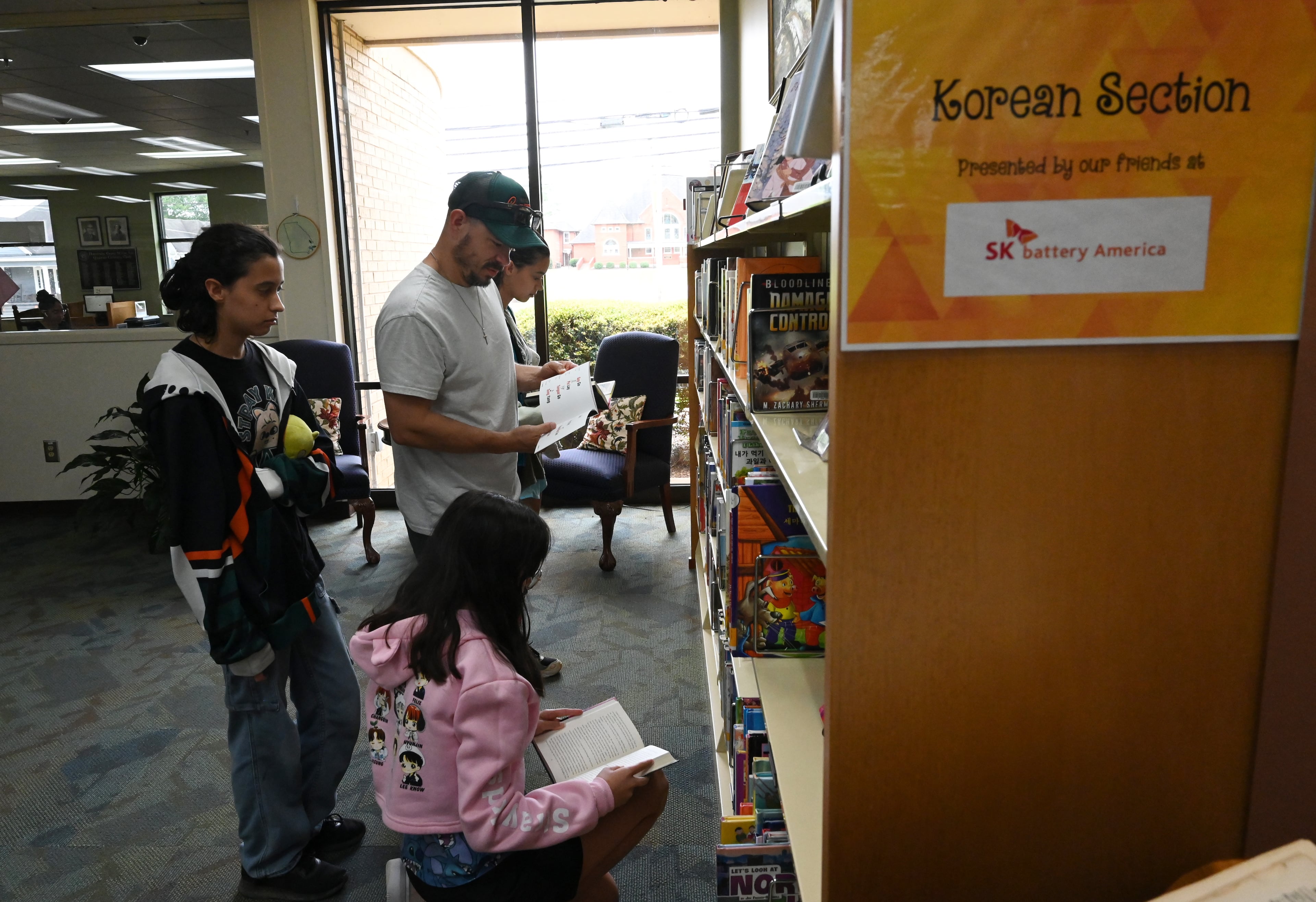 Jeff Gomez, of Charlotte, North Carolina, and his daughters, check out the Korean section inside the Commerce Public Library, Tuesday. The Gomezes stopped by the library on their way to Atlanta to attend a K-pop concert. SK Battery sponsored the Korean section at the library. (Hyosub Shin/AJC)