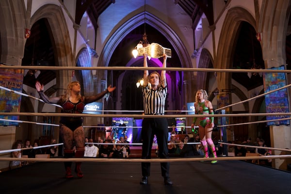 Referee Katie Crosby holds up the contested belt before Tiara's bout against Sarlett, left, during a Kingdom Wrestling show at St Peter's Church in Shipley, Saturday, March 29, 2025. (AP Photo/Jon Super)