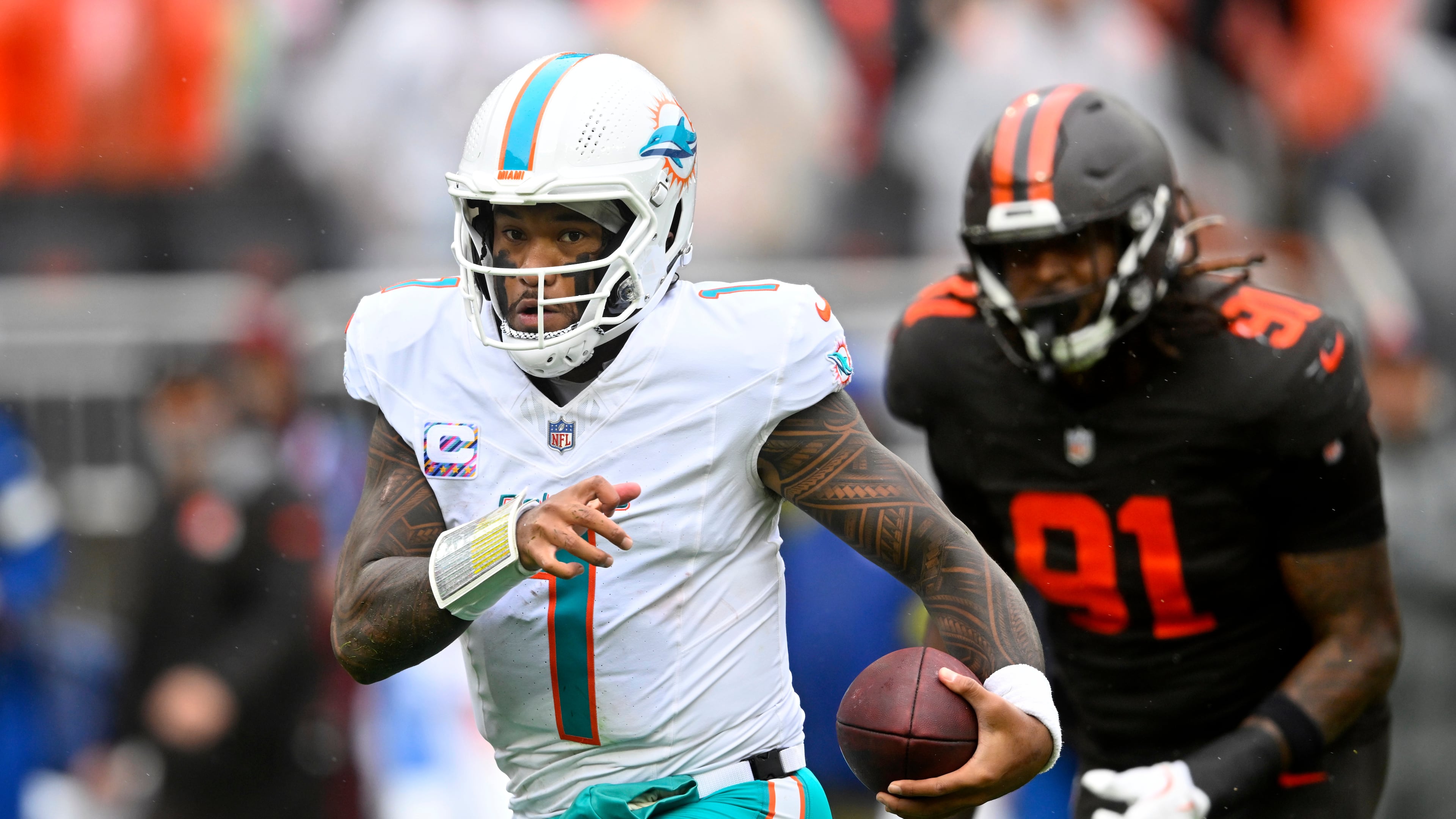 Miami Dolphins quarterback Tua Tagovailoa (1) scrambles from Cleveland Browns defensive end Alex Wright (91) in the first half of an NFL football game in Cleveland, Sunday, Oct. 19, 2025. (AP Photo/David Richard)