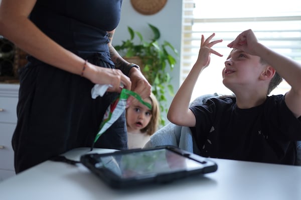 Charlie Lamb, right, who is diagnosed with autism and is non-verbal, uses an AAC device to communicate with his mother Eileen Lamb left, who also has autism, as Charlie's sister Billie looks on, Monday, May 12, 2025, in Austin, Texas. (AP Photo/Eric Gay)