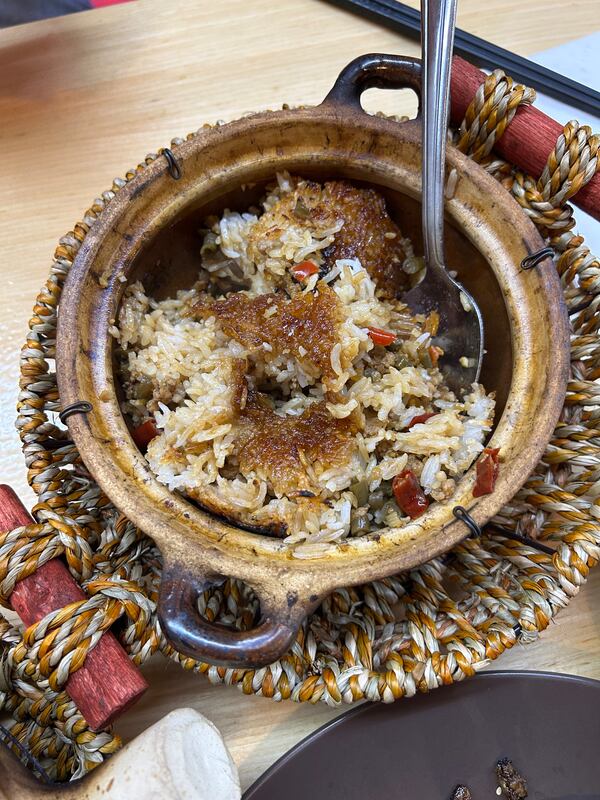 Golden, crispy rice in a claypot on a woven hot mat on top of a wooden table.