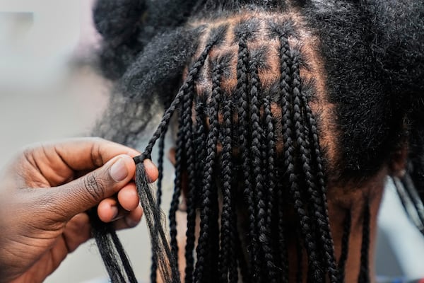 A braider at Eve's African Braiding in College Park, Ga., feeds in synthetic braiding hair while styling client Sadajah Herring's hair into knotless braids, Tuesday, May 6, 2025. (AP Photo/Stephanie Scarbrough)
