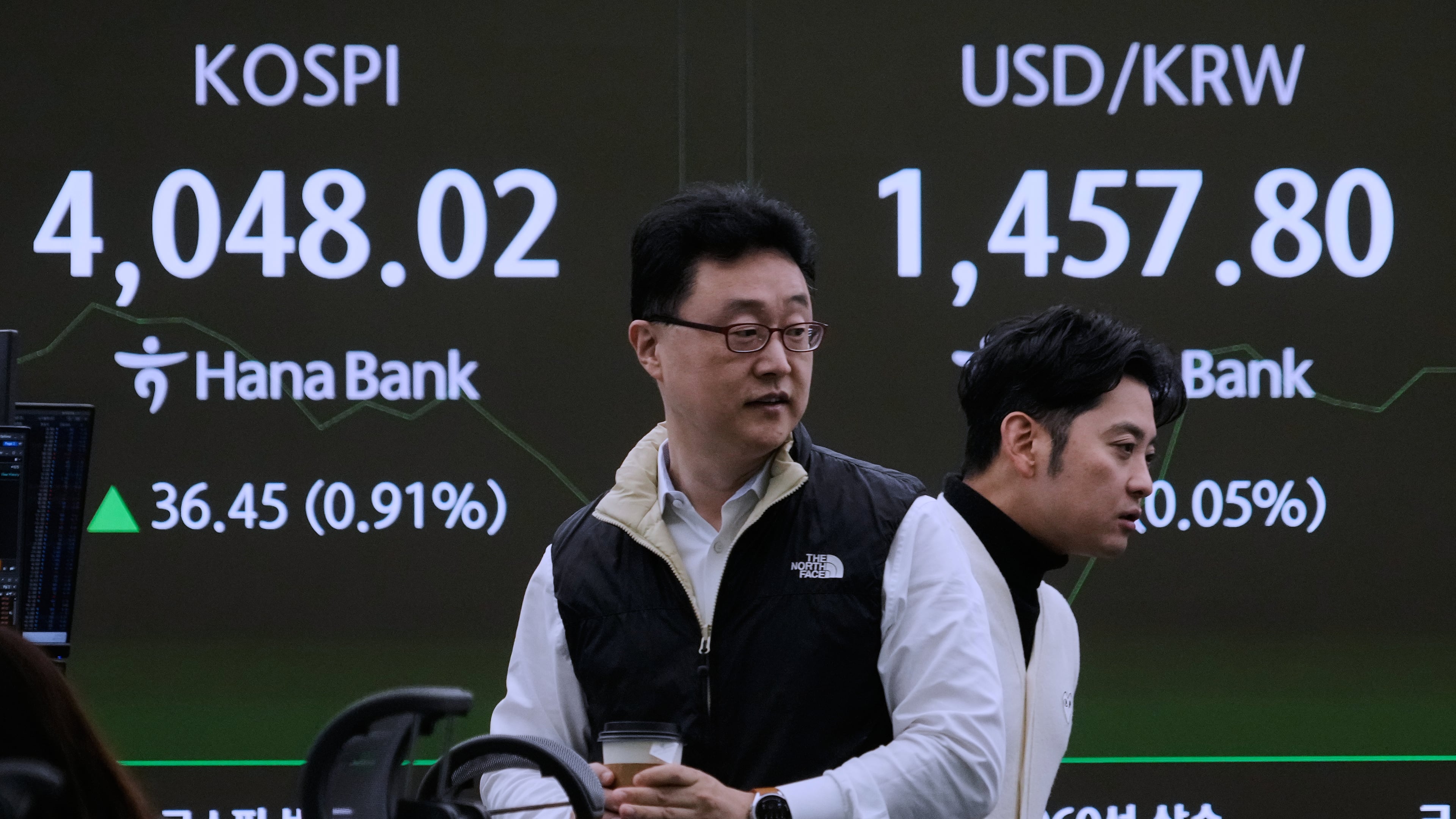Currency traders pass by a screen showing the Korea Composite Stock Price Index (KOSPI), left, and the foreign exchange rate between U.S. dollar and South Korean won at the foreign exchange dealing room of the Hana Bank headquarters in Seoul, South Korea, Monday, Nov. 17, 2025. (AP Photo/Ahn Young-joon)
