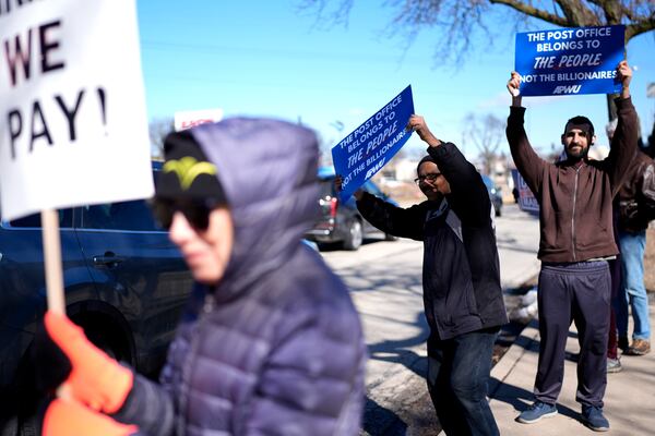 Madish Shah, center, and Abdul Abderrazzaq, right, hold signs during a demonstration outside of the United States Postal Service in Arlington Heights, Ill., Thursday, March 20, 2025. (AP Photo/Nam Y. Huh)