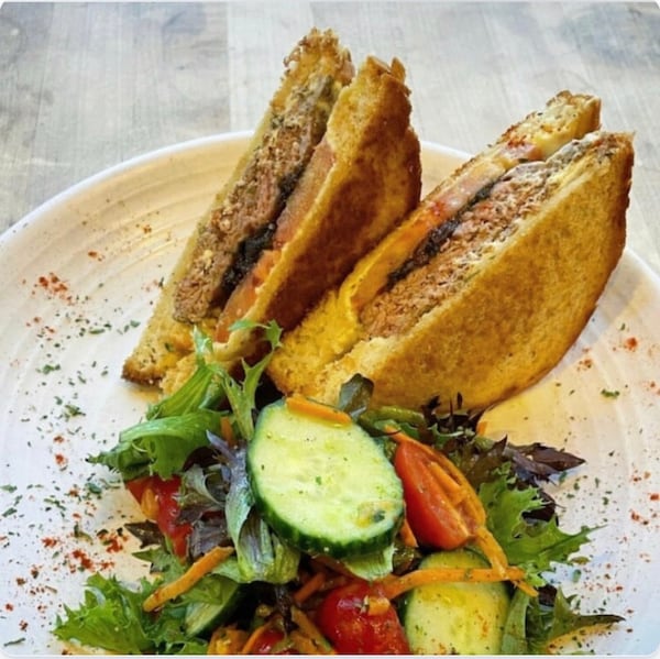 A patty melt (sliced in half) is served with a side garden salad on a plate garnished with a sprinkle of herbs.