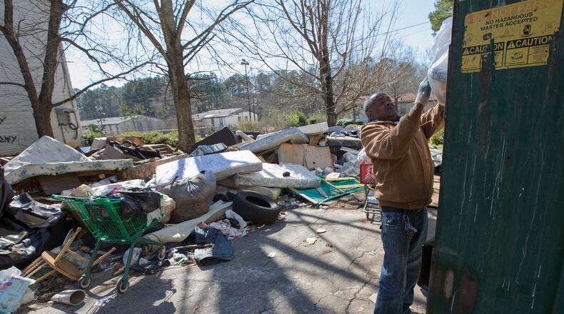 Despite the piles of trash, furniture and tires around him, James Starr, who has lived at Brennon Hill for four years, puts his trash in a Dumpster on Feb. 2. Ben Gray / bgray@ajc.com