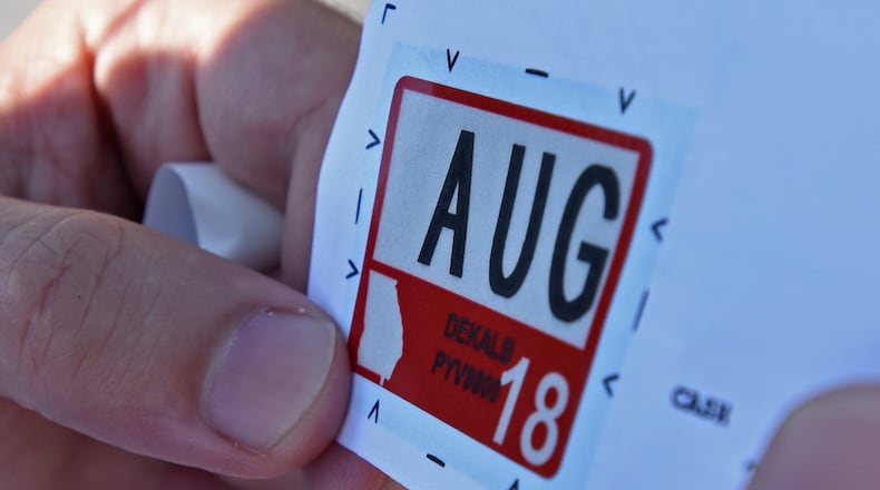 Mohamed Al Ali holds a registration sticker before he attaches it to his license plate in the parking lot of the Motor Vehicle Division of the DeKalb County Tax Commissioner North Office on Wednesday, July 26, 2017. HYOSUB SHIN / HSHIN@AJC.COM