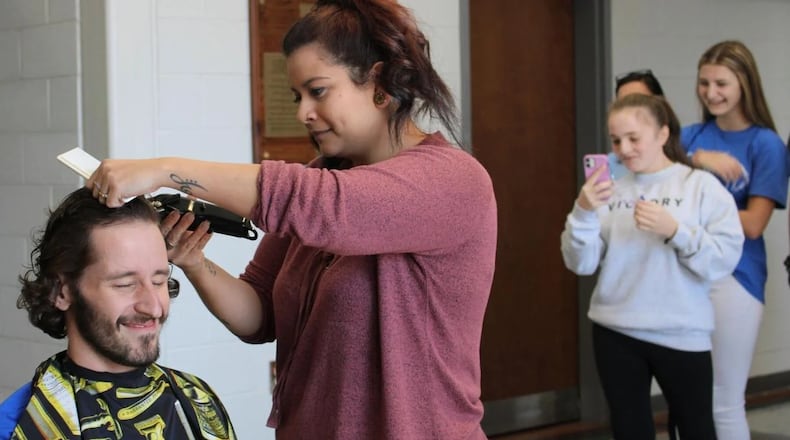 Model High School teacher Robert Murdock closes his eyes while he begins to get a mohawk haircut by Scarlett Gaddis of Lisa’s Salon in the atrium of Model High School on Friday morning. (Photo Courtesy of Adam Carey/Rome News-Tribune)