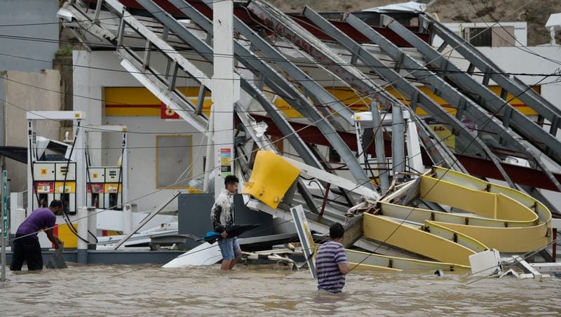 People walk next to a gas station flooded and damaged by the impact of Hurricane Maria, which hit the eastern region of the island, in Humacao, Puerto Rico, Wednesday, September 20, 2017. The strongest hurricane to hit Puerto Rico in more than 80 years destroyed hundreds of homes, knocked out power across the entire island and turned some streets into raging rivers in an onslaught that could plunge the U.S. territory deeper into financial crisis. (AP Photo/Carlos Giusti)