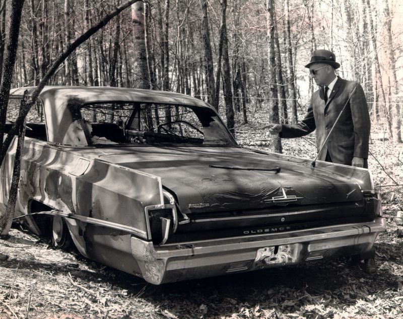 FBI agent Barney Ragsdale points to a burned, stolen car found near the scene where three Gwinnett policemen were slain in April 1964. The Gwinnett County Police officers slain were Jerry R. Everett, Marvin Jesse 'Pop' Gravitt and Ralph K. Davis. (MARION JOHNSON/AJC File)