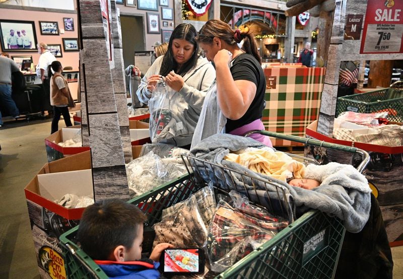 Black Friday shoppers Jennifer Lopez (center left) and her mother,  Veronica, search for special Black Friday discounts as their nephews Mizael (foreground), 6, and Mathew, 1-month old, ride on a shopping cart at the Bass Pro Shops at Sugarloaf Mills in Lawrenceville on Friday, November 25, 2022. (Photo: Hyosub Shin / Hyosub.Shin@ajc.com)
