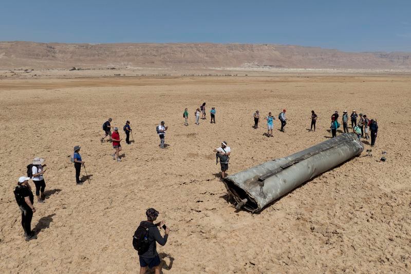 People gather around a component from an intercepted ballistic missile that fell near the Dead Sea in Israel, Saturday, April 20, 2024. Open fighting between Israel and Iran began April 1 with the suspected Israeli killing of Iranian generals at an Iranian diplomatic compound in Syria. That prompted Iran's retaliatory barrage last weekend of more than 300 missiles and drones that the U.S., Israel and regional and international partners helped bat down without significant damage in Israel. And then came Friday's strikes that hit near military and nuclear targets in Iran. (AP Photo/Itamar Grinberg)