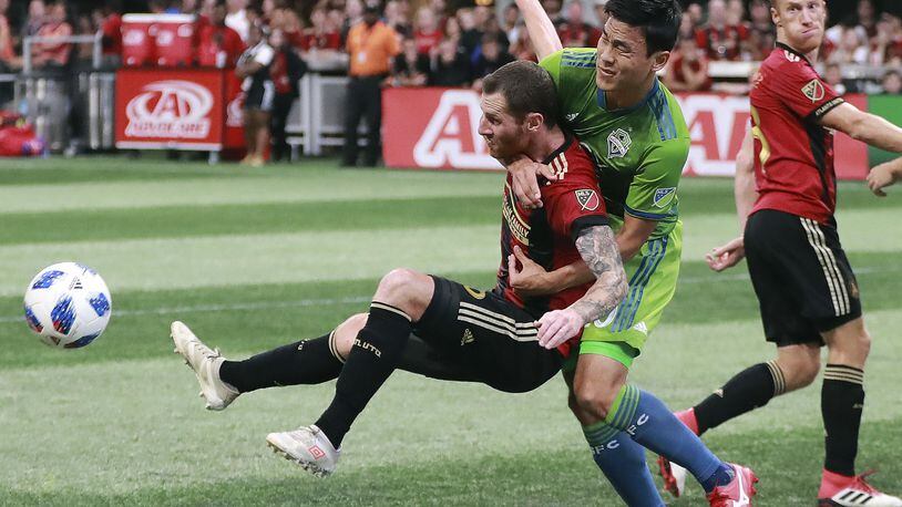 Atlanta United midfielder Chris McCann, left, is collared by Seattle Sounders defender Kim Kee-Hee during the first half of an MLS soccer game Sunday, July 15, 2018, in Atlanta.