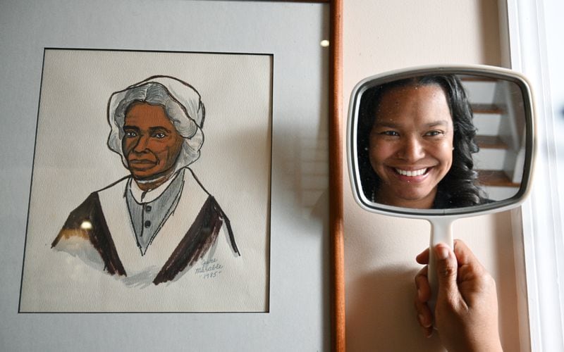 Sojourner Grimmett poses in front of a drawing of Sojourner Truth that was drawn by her grandmother at her home, Thursday, Feb. 2, 2023, in Atlanta. Sojourner Grimmett was named after Sojourner Truth by her father, a noted scholar of black studies and biographer of Malcolm X. She says the name has had an impact on her life and her career. (Hyosub Shin / Hyosub.Shin@ajc.com)