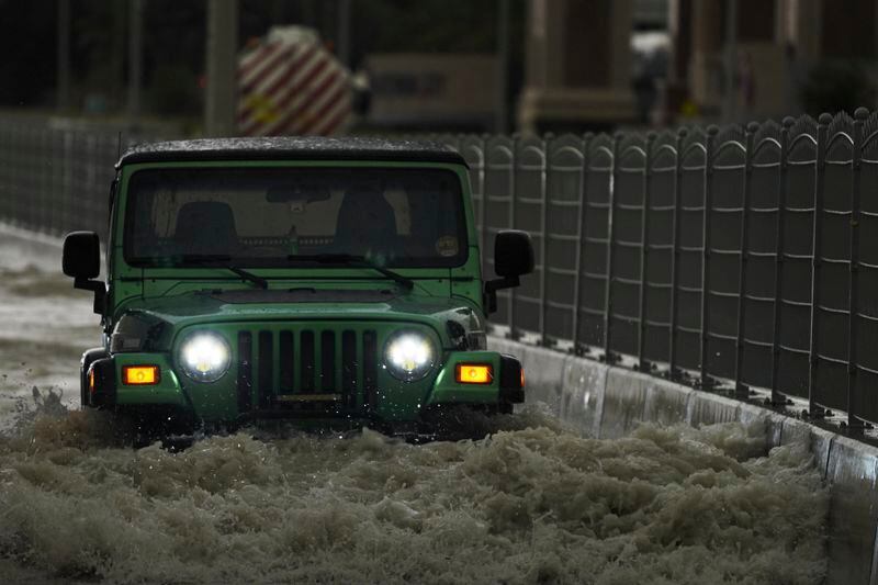 An SUV passes through standing water in Dubai, United Arab Emirates, Tuesday, April 16, 2024. Heavy rains lashed the United Arab Emirates on Tuesday, flooding out portions of major highways and leaving vehicles abandoned on roadways across Dubai. Meanwhile, the death toll in separate heavy flooding in neighboring Oman rose to 18 with others still missing as the sultanate prepared for the storm. (AP Photo/Jon Gambrell)