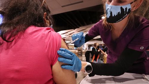 Veena Kalale gets a Pfizer vaccine shot from Fulton County Board of Health registered nurse Greer Pearson at the mass vaccination site at Mercedes-Benz Stadium last week. (Curtis Compton / Curtis.Compton@ajc.com)