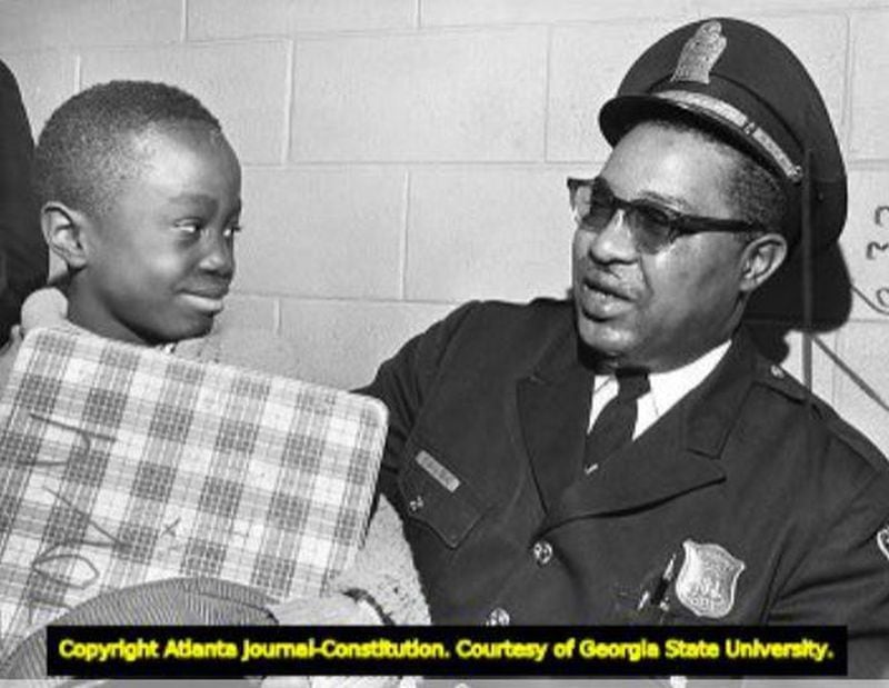 Ernest H. Lyons, one of the city's first Black police officers, sits with a child in 1968. 
(AJC File Photo)
