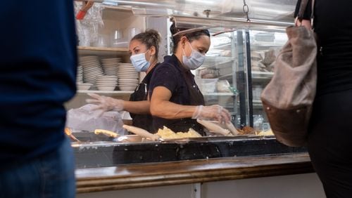 Ingred Cruez (left) and Marie Rodriguez help customers from behind acrylic panels during the lunch rush at Matthews Cafeteria on Main Street in Tucker.  Ben Gray for The Atlanta Journal-Constitution