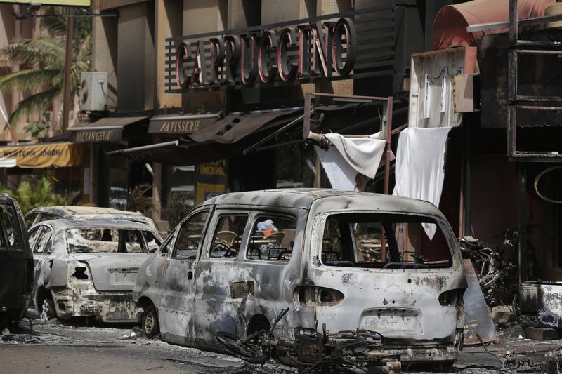 In this Sunday Jan. 17, 2016, file photo, burnt cars are seen outside the Cappuccino Cafe that was attacked by jihadists in Ouagadougou, Burkina Faso. Gaetan Santomenna lost his wife, his 9-year-old son and his mother the night jihadists attacked his cafe in Burkina Faso's capital before striking a nearby hotel. More than a year later, he was reopening doors to the popular restaurant as a sign of resistance to the extremism growing in this West African country. (AP Photo/Sunday Alamba, File)