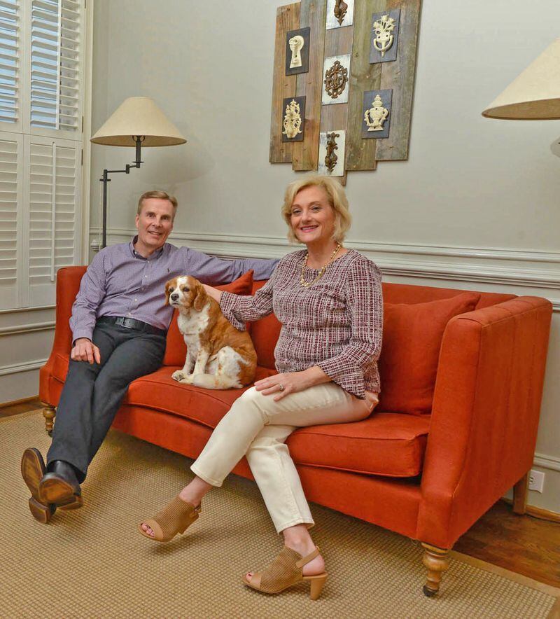 Jim and Kathy Callahan sit in their parlor with their King Charles spaniel, Charlie. Jim Callahan retired in 2017 as CEO of Ackerman Security Systems. The art piece is composed of antique door knockers that Kathy collected 20 years ago and were transformed into a piece of wall art by Ken Roberts of Retired Wood Kreations. The sofa and cabinet are from RH, and the walls are painted Sherwin-Williams Gateway Gray.