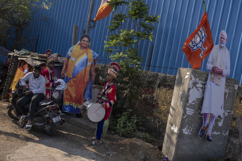 Members of a local band stand next to cutouts of Bharatiya Janata Party candidate Tamilisai Soundararajan and Prime Minister Narendra Modi, right, as they wait for her arrival for an election campaign rally, in the southern Indian city of Chennai, April 14, 2024. (AP Photo/Altaf Qadri)