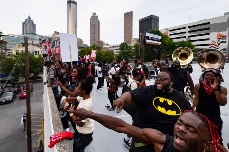 Zachary Nealy (in batman shirt) and Rashaad Horne, right, shout from a rooftop parking deck toward protesters at Centennial Olympic Park, as their band plays Saturday, June 6, 2020, in Atlanta. The musicians deicided to provide support through music to help give them a little extra energy. Protesters were demonstrating against the death of George Floyd at the knee of Minneapolis police. JOHN AMIS FOR THE ATLANTA JOURNAL-CONSTITUTION