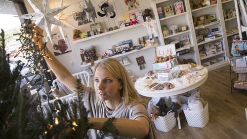 Brooke Henze of Sandy Springs places stringed lights onto a Christmas tree inside of her store, The Swell Shop.Henze spent the day decorating and organizing the shop ahead of this weekend’s Small Business Saturday. ALYSSA POINTER/ALYSSA.POINTER@AJC.COM