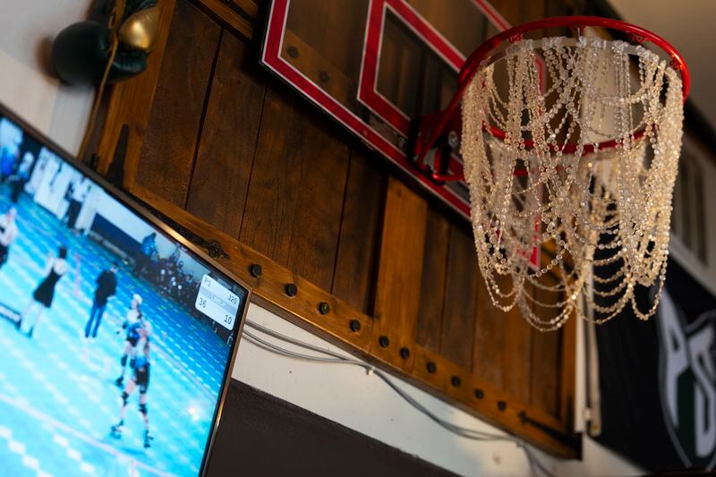 A roller derby match is played on a TV next to a decorated basketball hoop at The Sports Bra sports bar on Thursday, April 25, 2024, in Portland, Ore. (AP Photo/Jenny Kane)