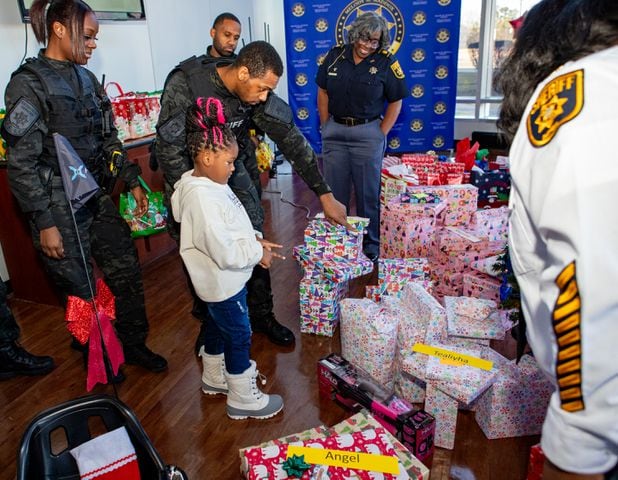 DeKalb County Sheriff’s Office holds the 16th annual Adopt-A-Family celebration on Tuesday, Dec 16, 2023 where 5-year-old Tealitha Height, gets a little help picking the gift she should open at the party. Law enforcement officers donate their own money and buy gifts for about a dozen local children.  (Jenni Girtman for The Atlanta Journal-Constitution)