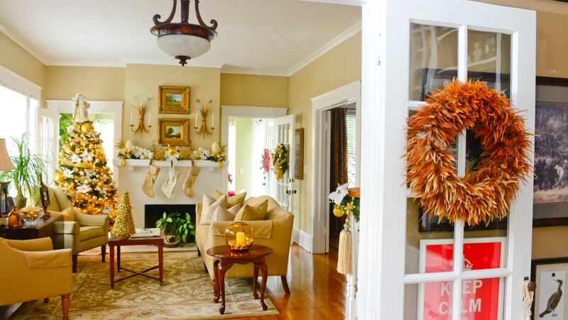 A rustic feather wreath on the door leading to the casual, earth-toned den contrasts with  the more formal adjacent living room, which is decorated in bright golds and whites.