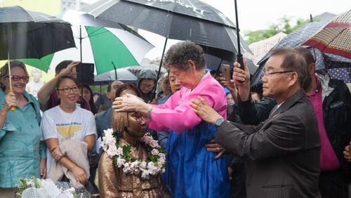 In a photo from the June 30 unveiling of the Comfort Women memorial statue in Brookhaven, Il-Chul Kang, 89, a Korean survivor of the atrocity, places her hands on the head of the bronze figure. Photo: David Kwon/The Korea Daily