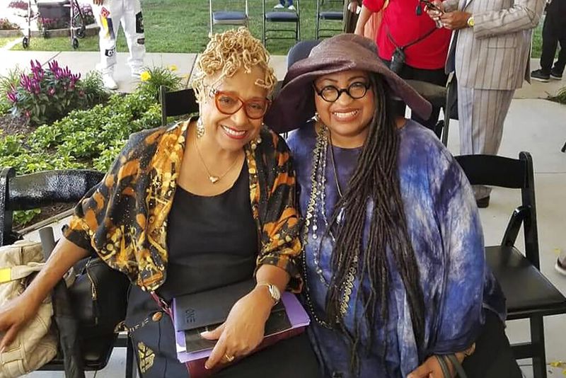 In this 2019 photo provided by Marsha Battle Philpot, Philpot, right, widely known by her moniker Marsha Music and Brenda Perryman pose for a photo at the groundbreaking ceremony for the Motown Museum expansion in Detroit. As the coronavirus tightened its grip across the country, it is cutting a particularly devastating swath through an already vulnerable population, black Americans. The coronavirus deaths in Detroit include educator and playwright Perryman and Gloria Smith, who was a staple at the cityâs African World Festival and died within a week of her husband. (Marsha Battle Philpot via AP)