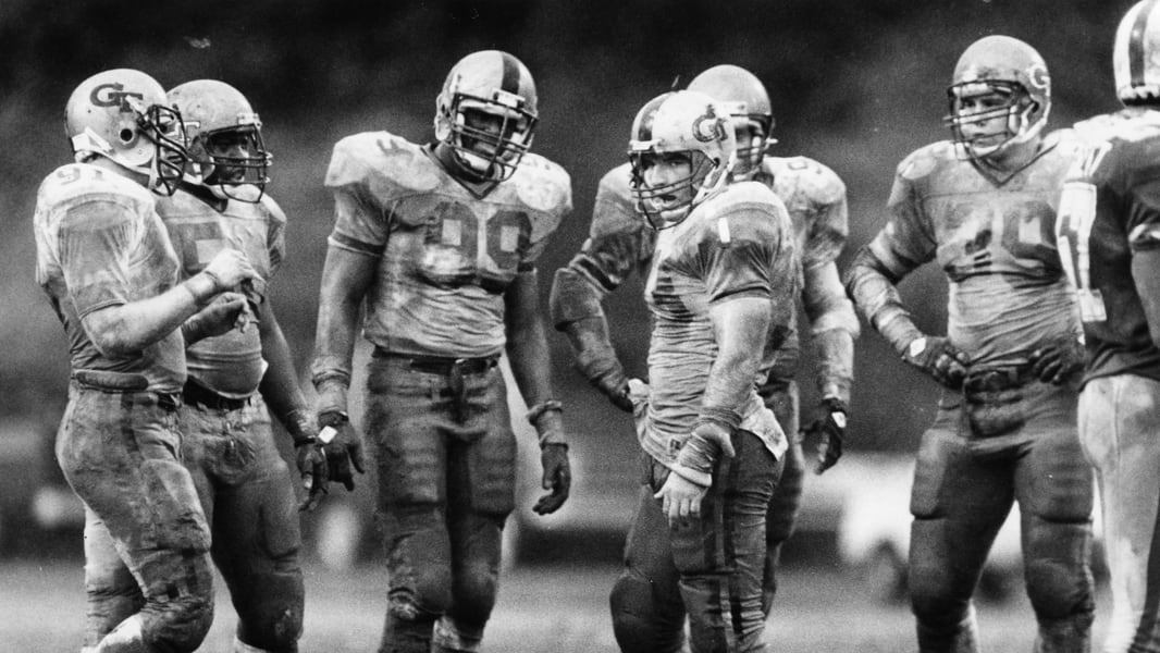 Ted Roof (center), Pat Swilling (99) and other Georgia Tech defensive players are soaked in mud during a game against Duke in 1985. They were the centerpieces of Georgia Tech's "Black Watch" defense that will be honored in Tech's matchup with Notre Dame Saturday with throwback uniforms. (Andy Sharp / AJC file)