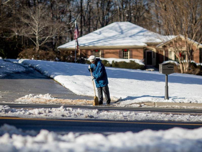 Ice and snow cover parts of Shiloh Road as Kathryn Cavan tries to clear her driveway of ice with a broom, Sunday, Dec. 10, 2017, in Kennesaw,