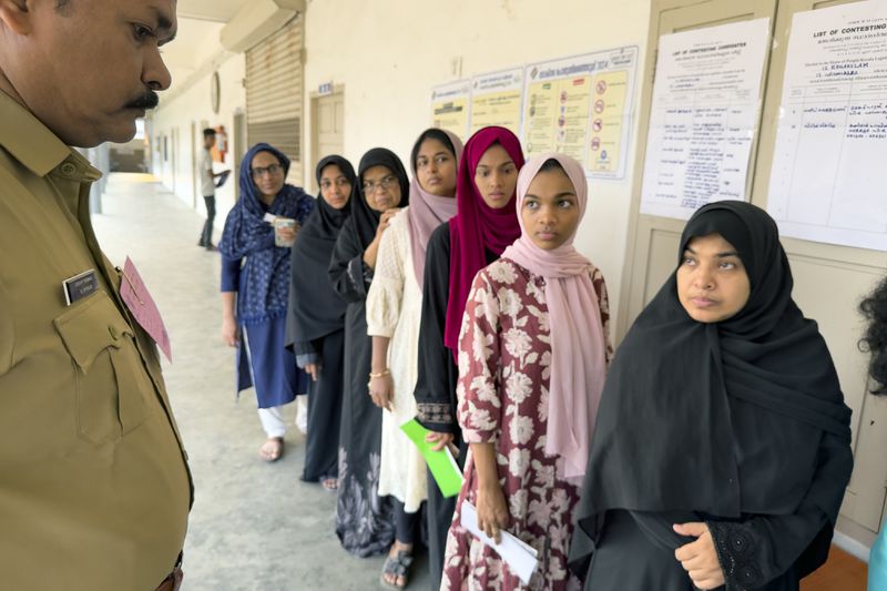 A policeman stands guard as people queue up to vote during the second round of voting in the six-week long national election outside a polling booth in Kochi, southern Kerala state, India, Friday, April 26, 2024. (AP Photo/R S Iyer)