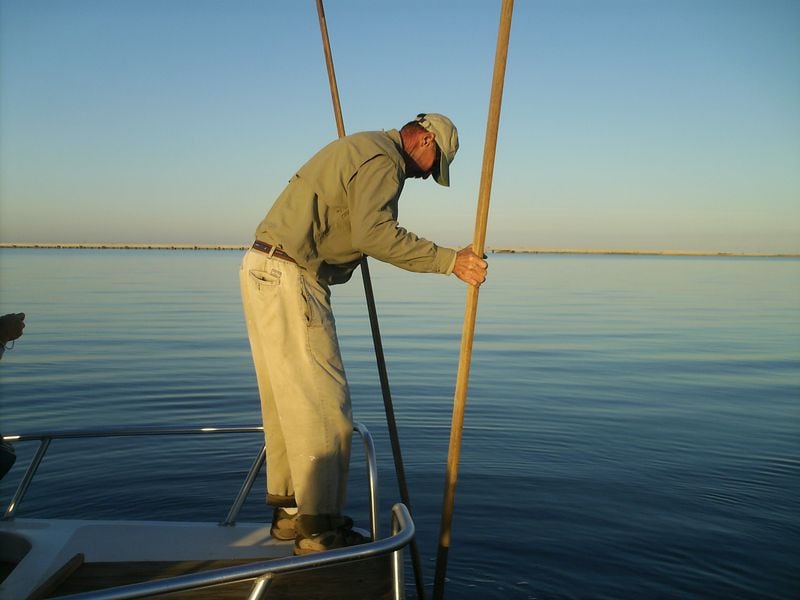 In this file photo, an oysterman works his oyster tongs in Apalachicola Bay near St. George Island. In the distance is the five-mile long bridge that connects the island to the mainland. Credit: Blake Guthrie
