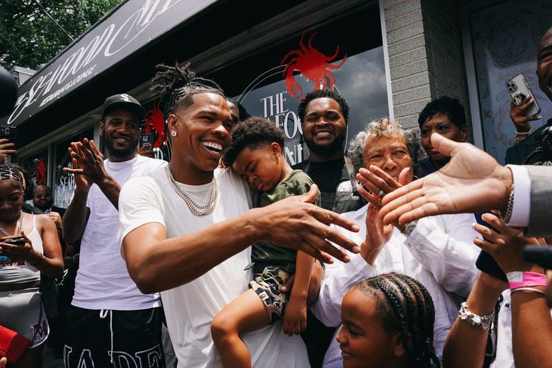 Rapper Lil Baby (center) holds his son, Loyal, as he shakes hands with City Councilman Byron Amos at the grand opening of his restautant, the Seafood Menu, in Atlanta, Georgia on Friday, July 14, 2023. (Olivia Bowdoin / Atlanta Journal-Constitution) 