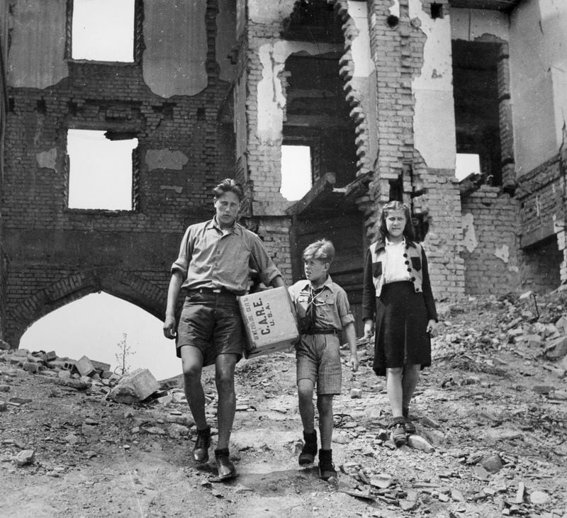 Over the rubble of war-battered Berlin, a father is carrying home a CARE food package that will relieve his family's needs while they wait for better times.